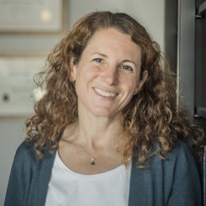 person looking forward and smiling, wearing green cardigan sweater and white blouse