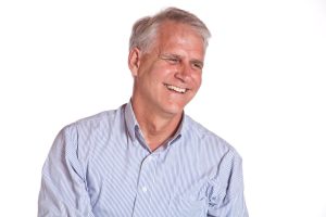 Professional man in a button-up shirt laughing in front of a white background.